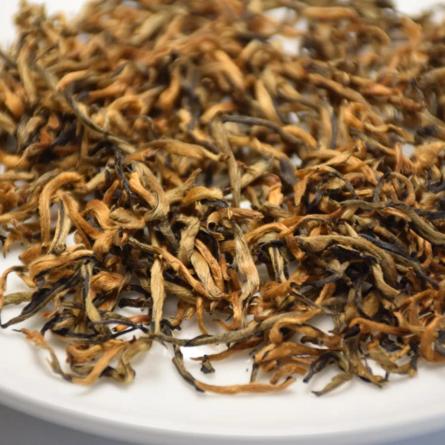 Close-up of premium Shaoguan Honey Black Tea dry leaves, showing abundant golden tips on a white plate.