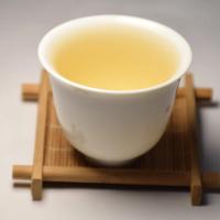Professional quality check of EU-compliant raw Pu-erh tea infusion, showing a crystal-clear, bright yellow liquor in a white cup.