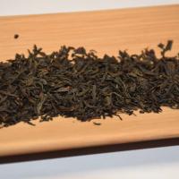 Quality inspection of wholesale Keemun Gongfu black tea, showing its signature tightly twisted and wiry dry leaves on a bamboo tray.