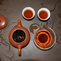 Professional tasting of wholesale organic ripe Pu-erh tea, showcasing a clear, dark red liquor in a glass pitcher and infused leaves in a clay teapot.