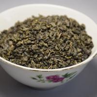 Professional presentation of wholesale organic Gunpowder green tea, showing tightly rolled dark green pellets in a traditional floral ceramic bowl.