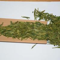 Professional quality inspection of wholesale Da Fo Longjing green tea, showing flat and straight dry leaves on a bamboo tea scoop.