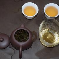 Authentic Chaozhou Phoenix Dan Cong Oolong in a white ceramic cup and tea scoop, highlighting the golden infusion and dark wiry leaves.