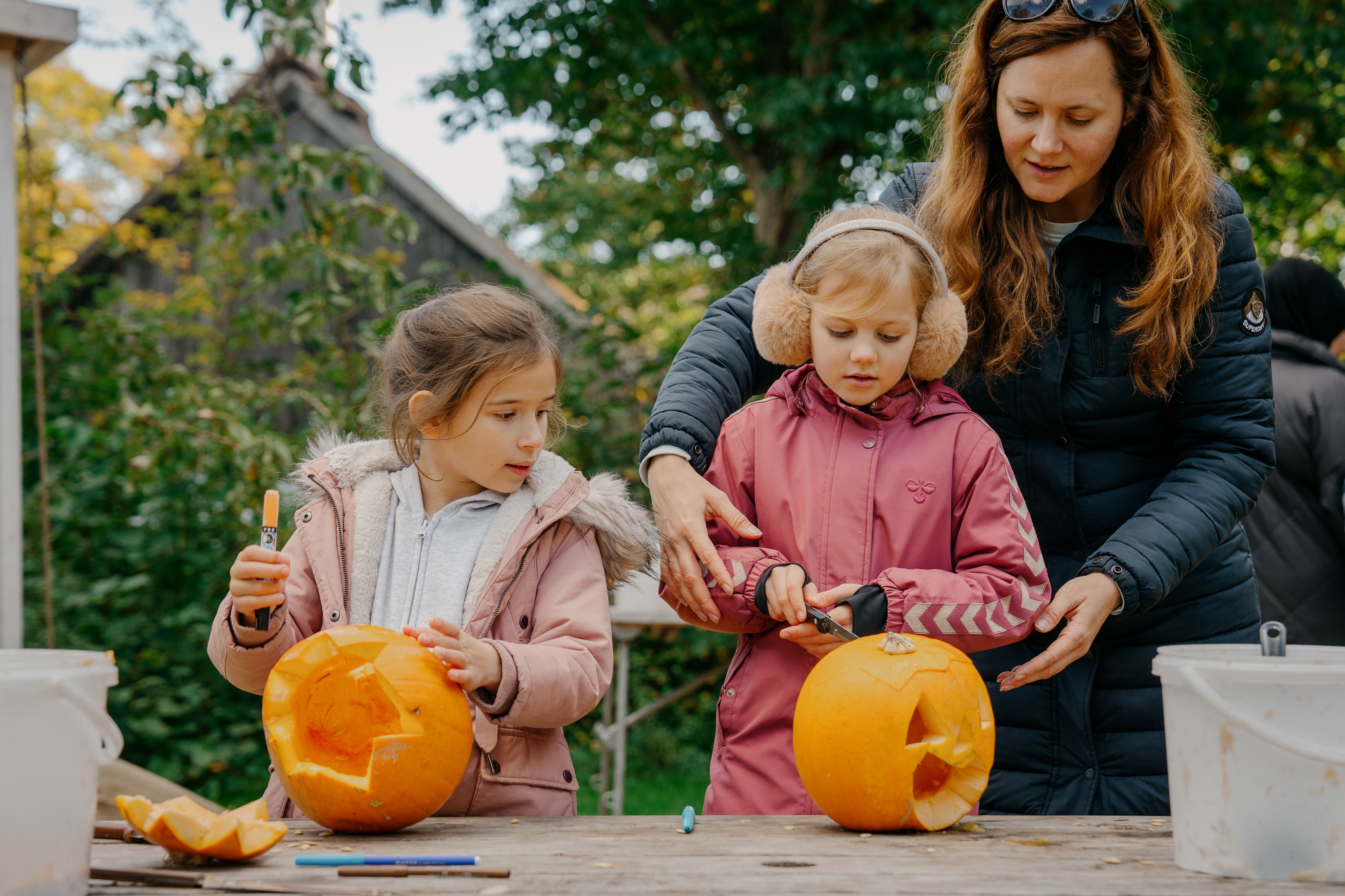 Mor og to piger skærer i hver deres græskar til Halloween.