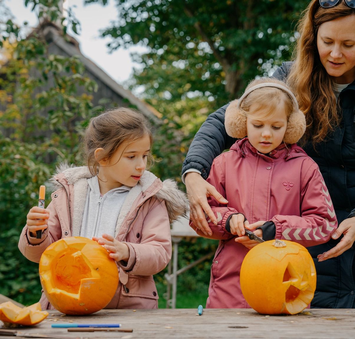 Mor og to piger skærer i hver deres græskar til Halloween.
