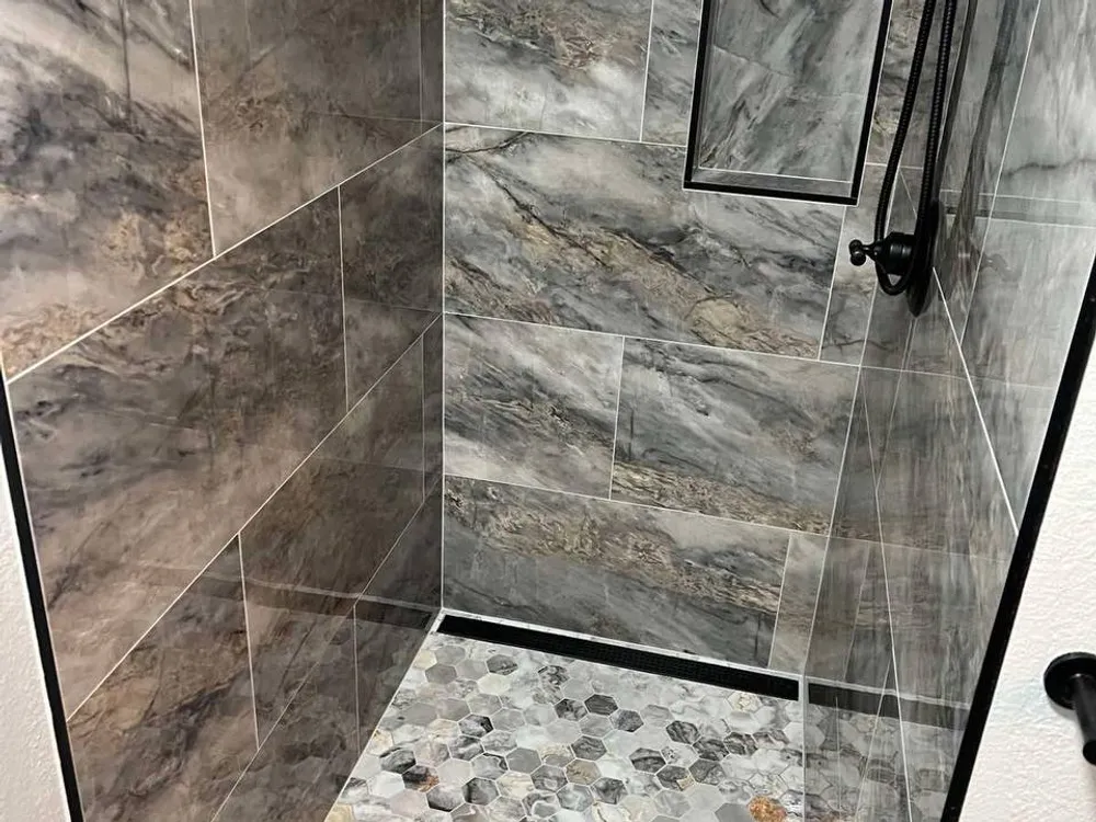 Marble-look porcelain tile shower with black fixtures and a mosaic niche
