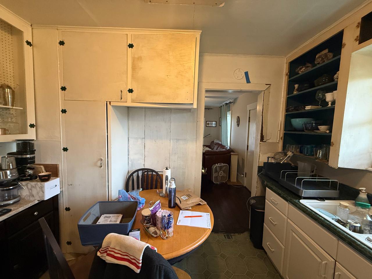 The South Seattle kitchen before the remodel: original cabinets with missing doors, a dining table in the middle and a wall to the living room