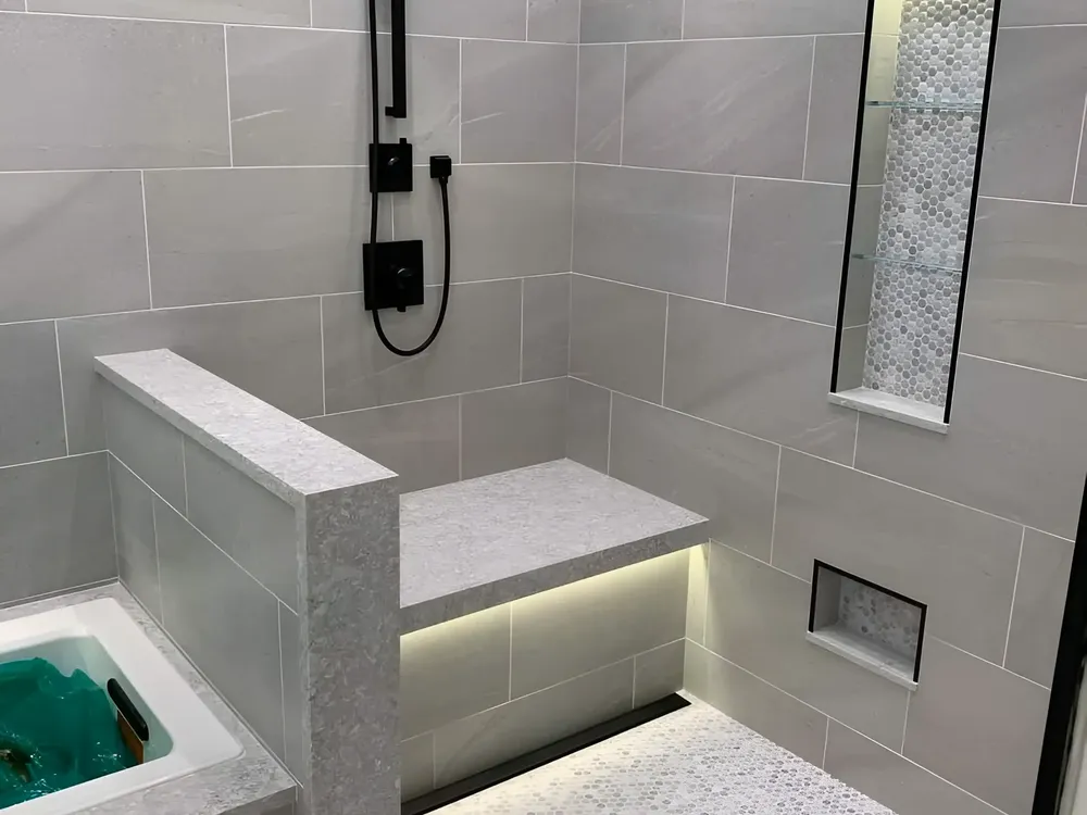 Gray tile shower with a bench, a niche and lighting