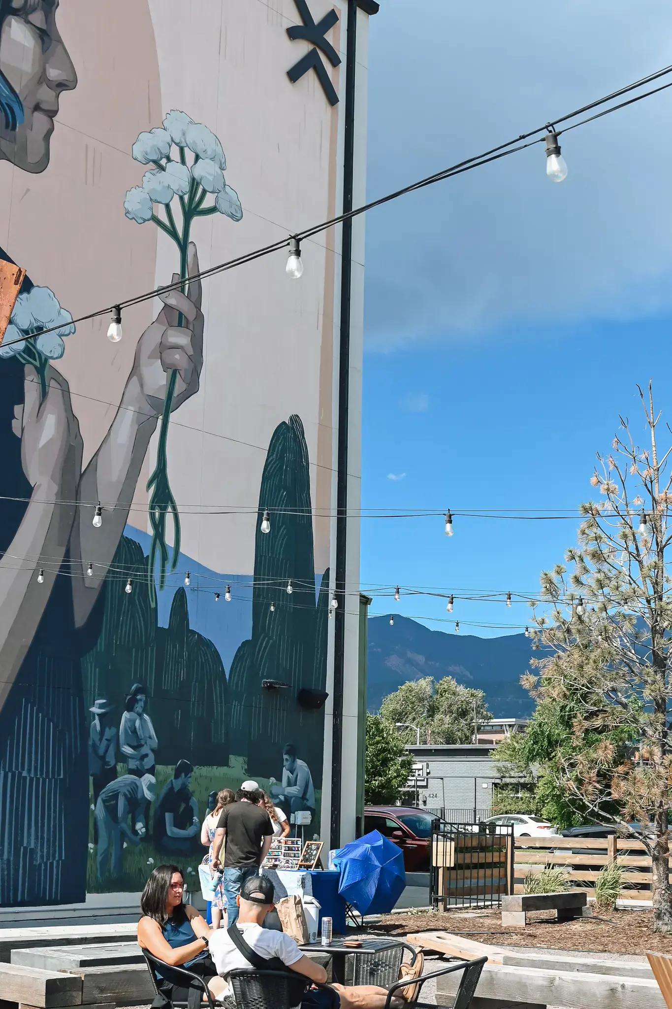 A mural on the side of a building with outdoor seating and a mountain view.