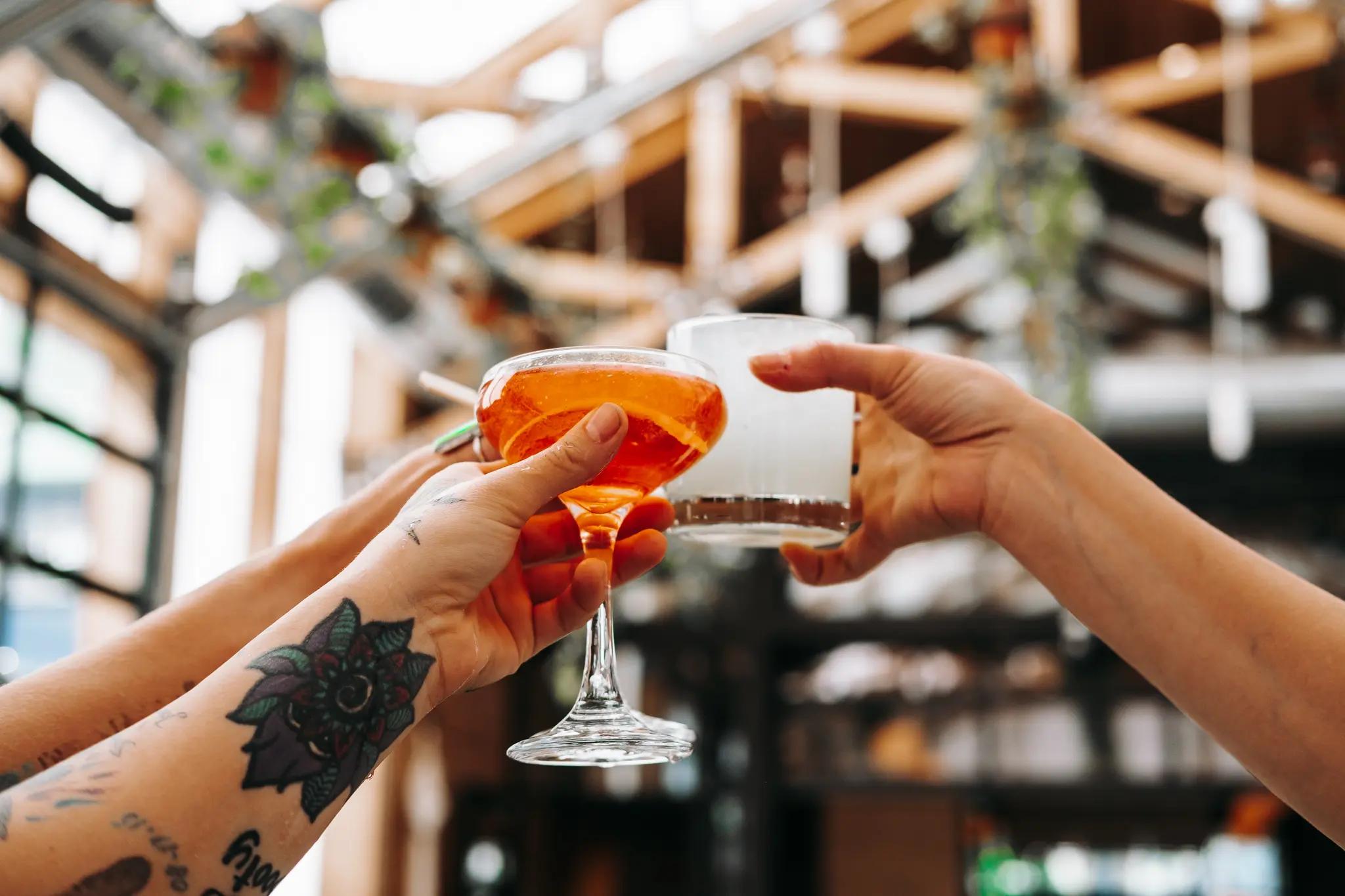Two hands holding up cocktail glasses in a bar