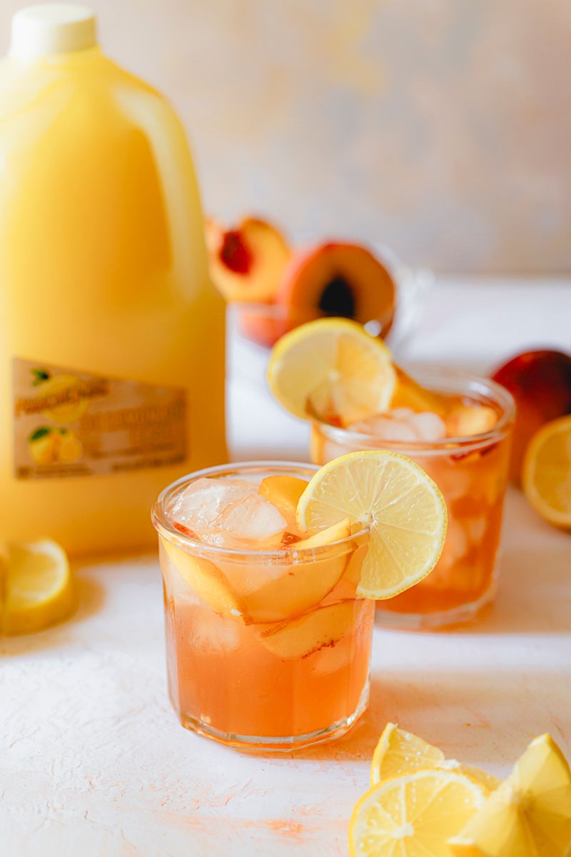 Peachy Arnold Palmer made with Perricone Farms Lemonade Base and peach tea, served over ice and garnished with fresh peach, lemon, and mint