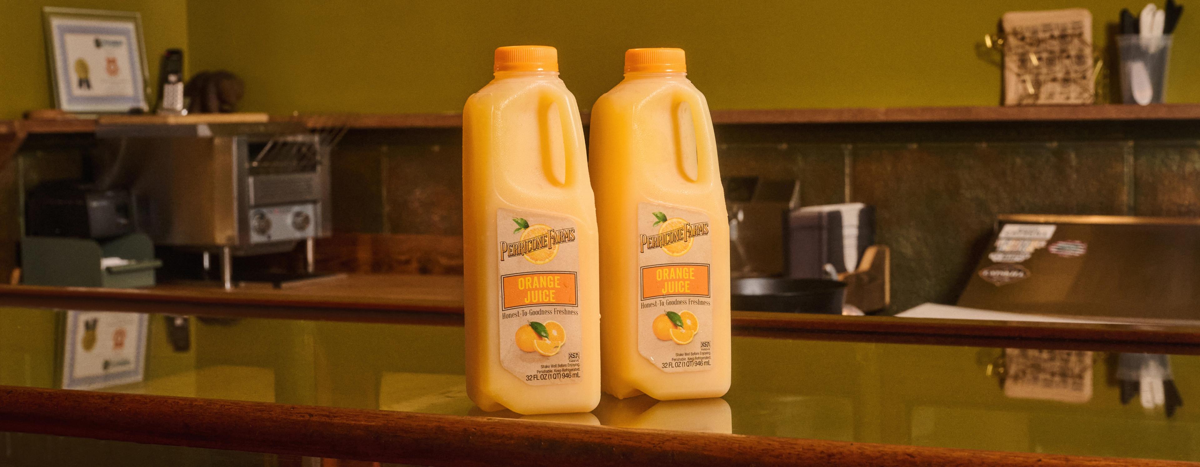 Two 64 oz. bottles of Perricone Farm's Orange Juice sat atop a restaurant bar ready to be poured for customers or guests