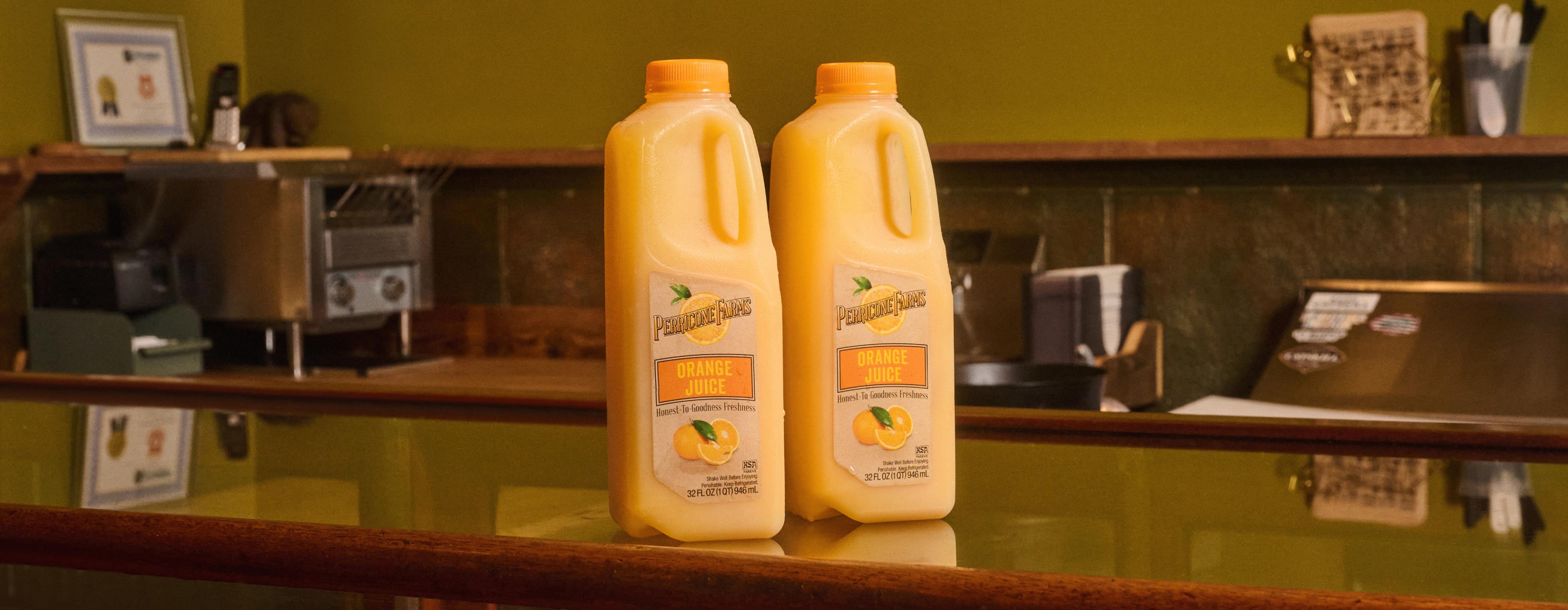 Two 64 oz. bottles of Perricone Farm's Orange Juice sat atop a restaurant bar ready to be poured for customers or guests