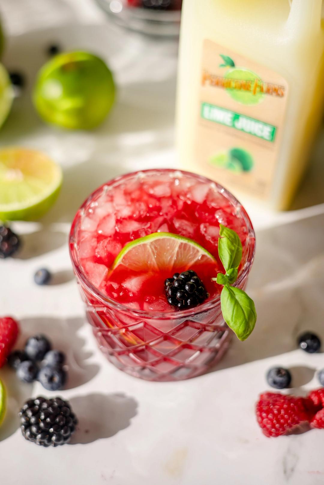 Mixed Berry Smash made with Perricone Farms Lime Juice, vodka, and muddled berries, served over ice and garnished with lime, blackberry, and fresh basil