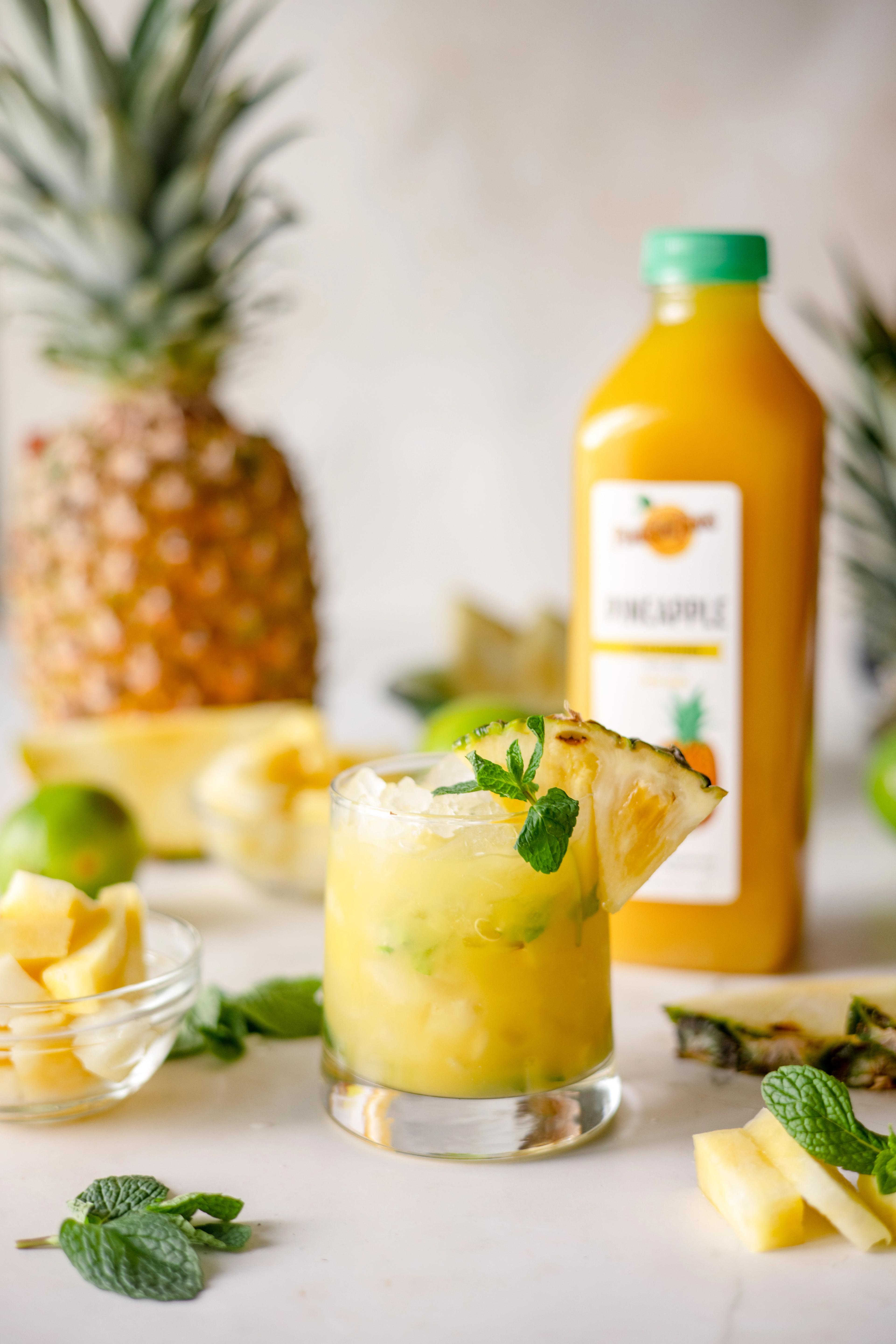 Pineapple Mojito Mocktail made with Perricone Farms Pineapple Juice, mint, and lime, served over ice with fresh pineapple and club soda in a short glass