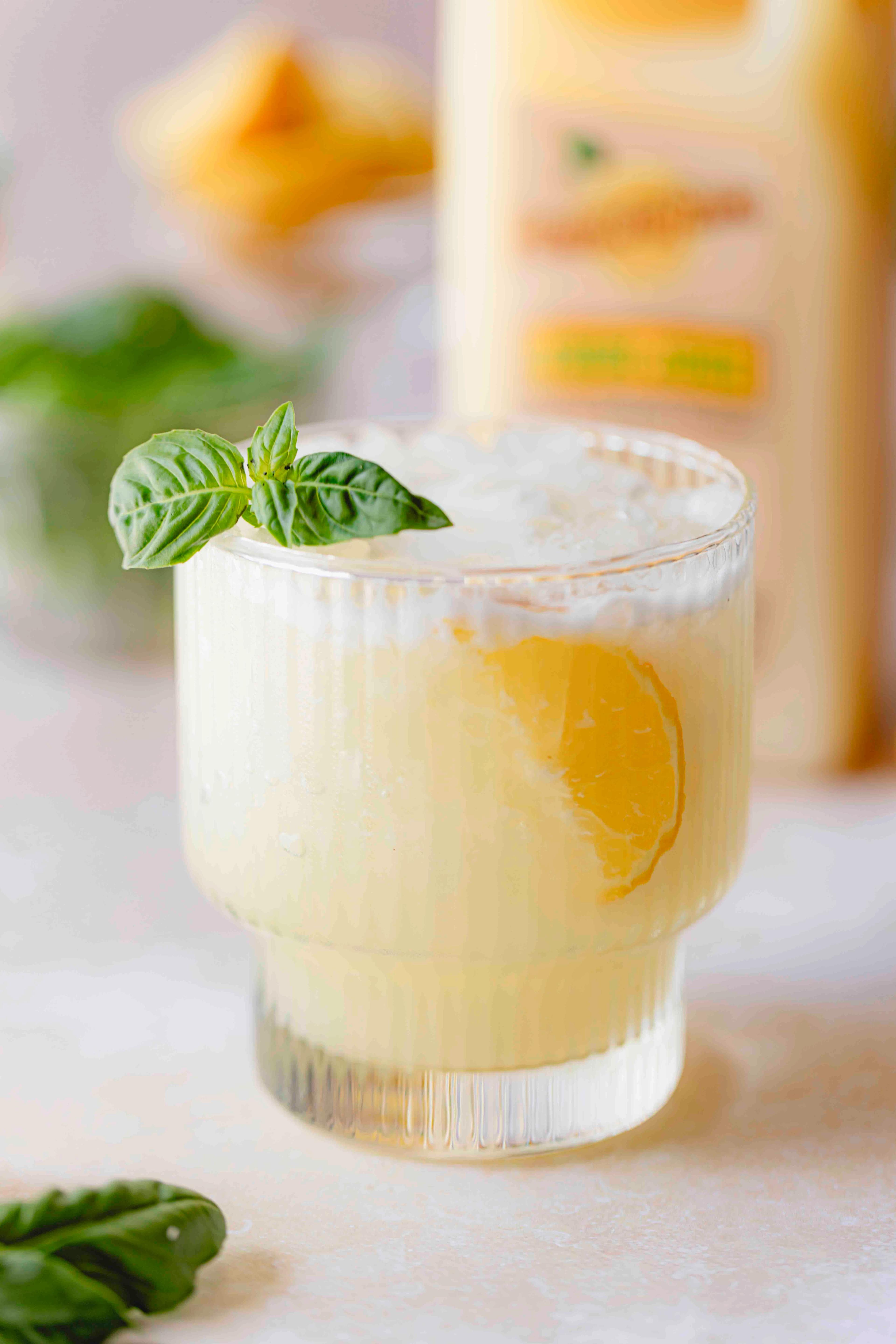 Lemon Basil Fizz made with Perricone Farms Lemon Juice, gin, and egg white served over ice with basil garnish beside a jug of lemon juice and fresh herbs
