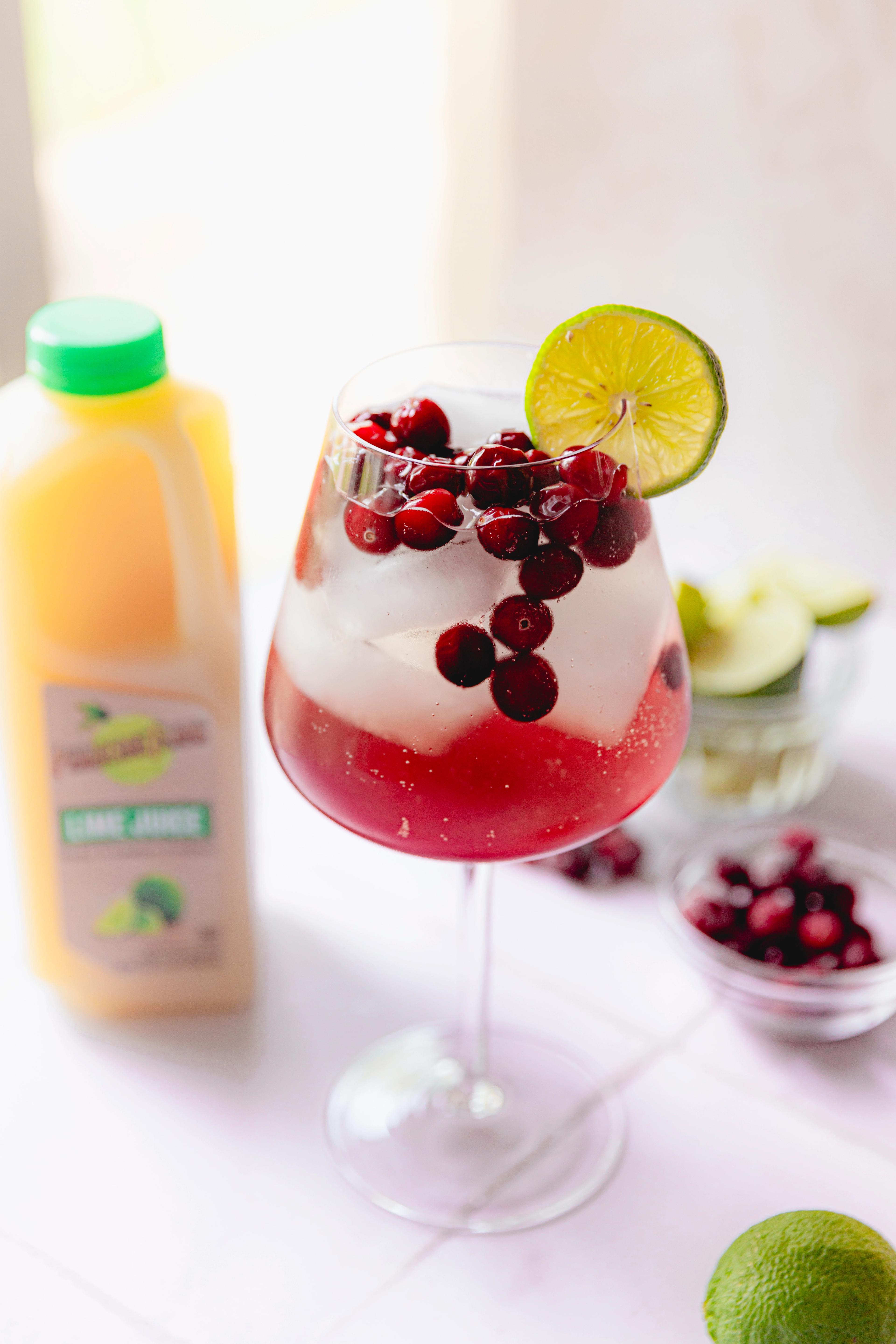 Elderflower Cranberry Lime Spritz made with Perricone Farms Lime Juice, cranberry juice, and elderflower liqueur, served over ice with frozen cranberries and lime