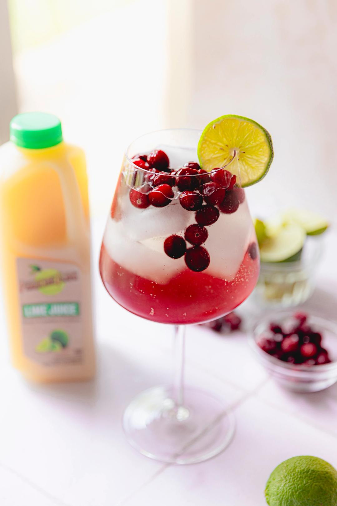 Elderflower Cranberry Lime Spritz made with Perricone Farms Lime Juice, cranberry juice, and elderflower liqueur, served over ice with frozen cranberries and lime