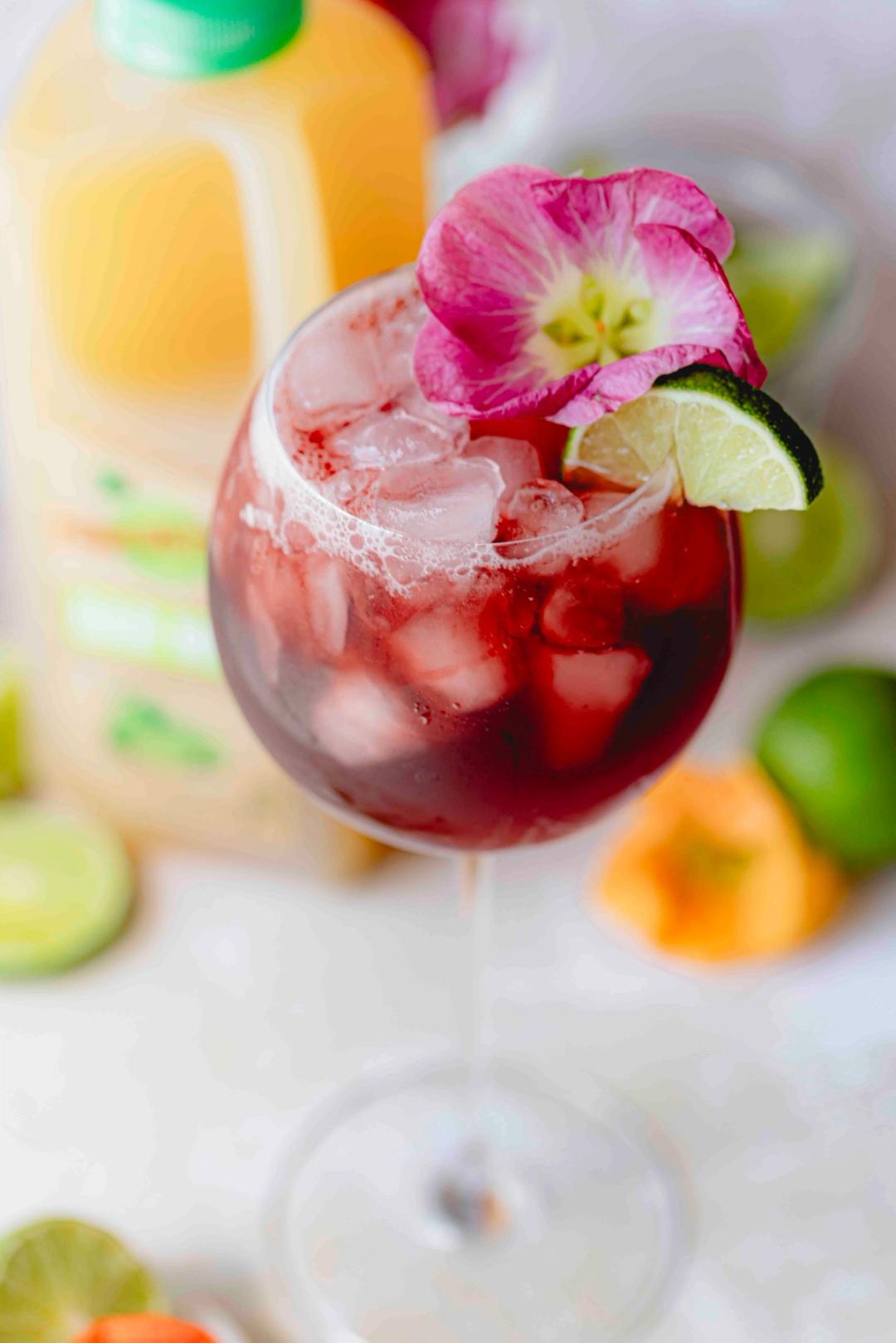 Hibiscus Margarita made with Perricone Farms Bar Mix, tequila, and hibiscus syrup served over ice in a stemmed glass, garnished with lime and an edible flower