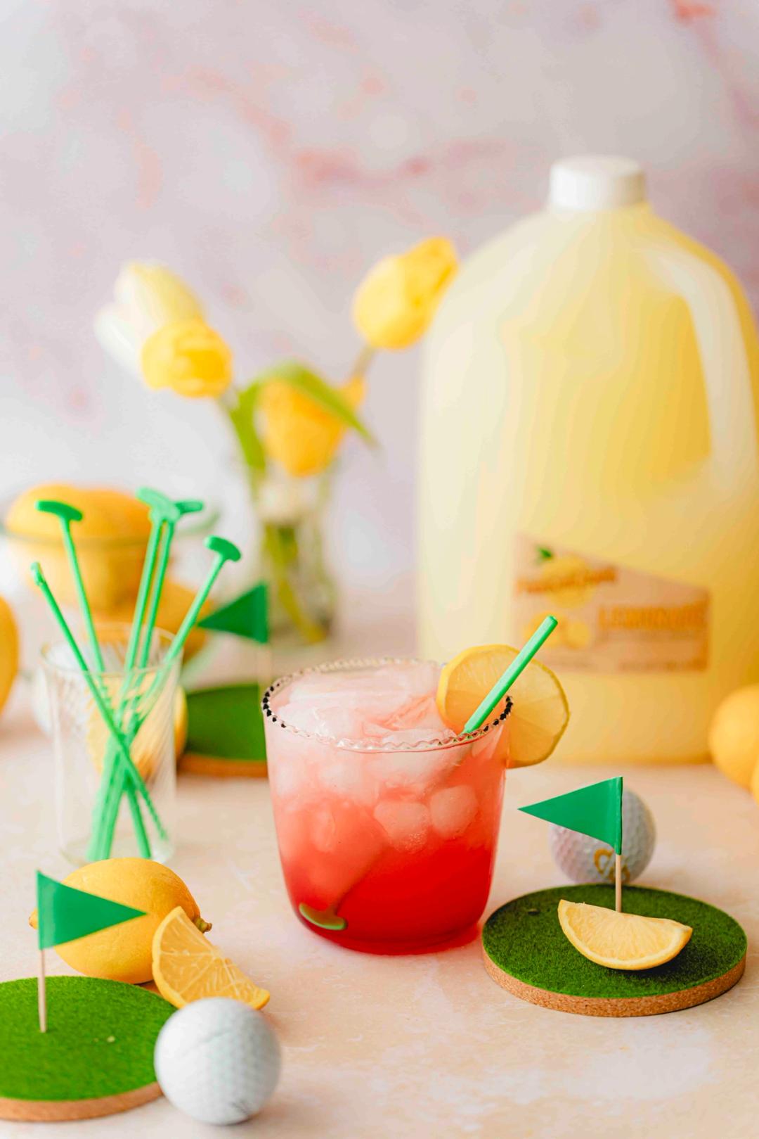 Classic Azalea Cocktail made with Perricone Farms Lemonade, vodka, and grenadine over ice, garnished with lemon and styled with golf-themed accents and fresh lemons