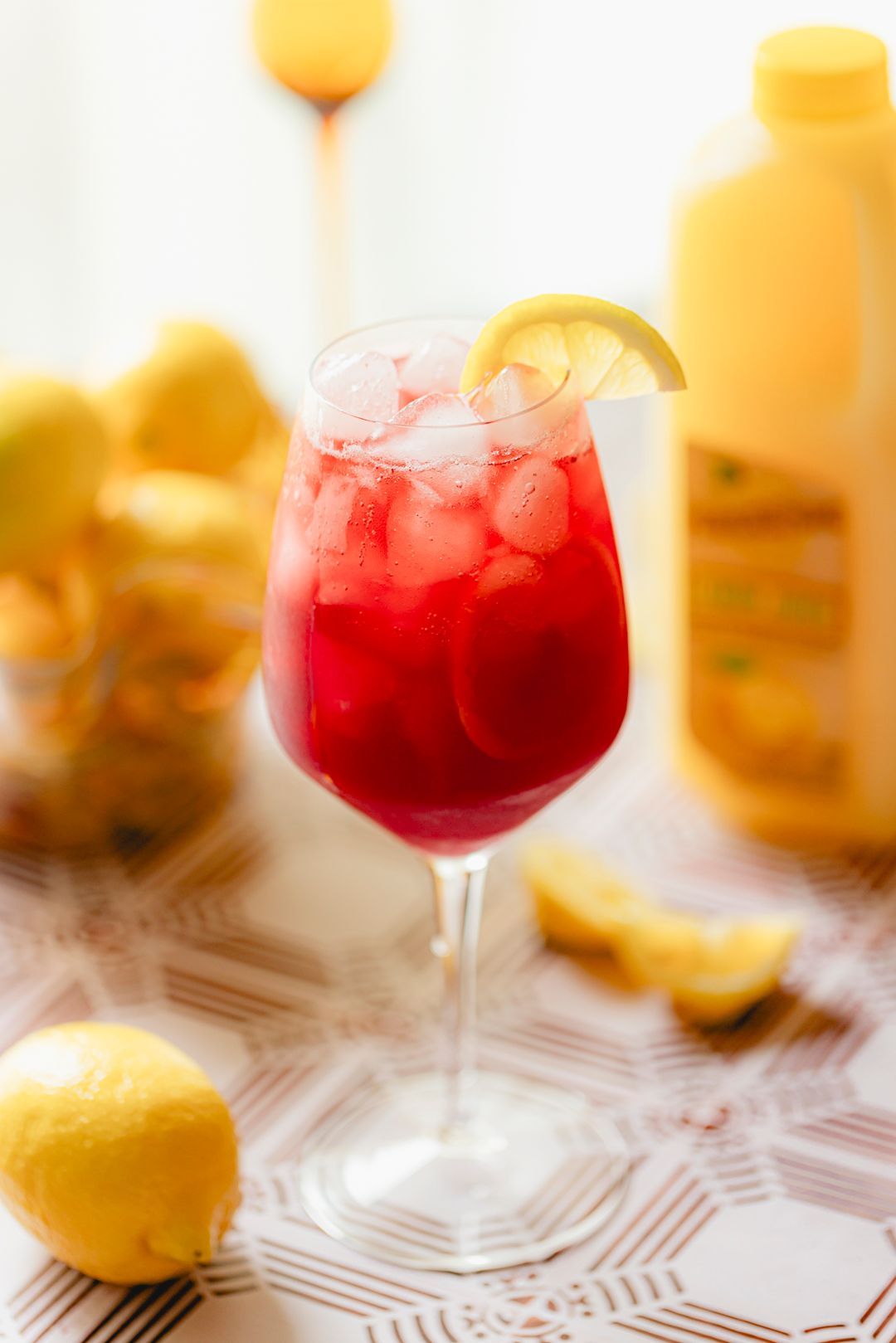 Classic Tinto de Verano made with Perricone Farms Lemon Juice, red wine, and lemon-lime soda, served over ice in a wine glass with lemon wedge garnish