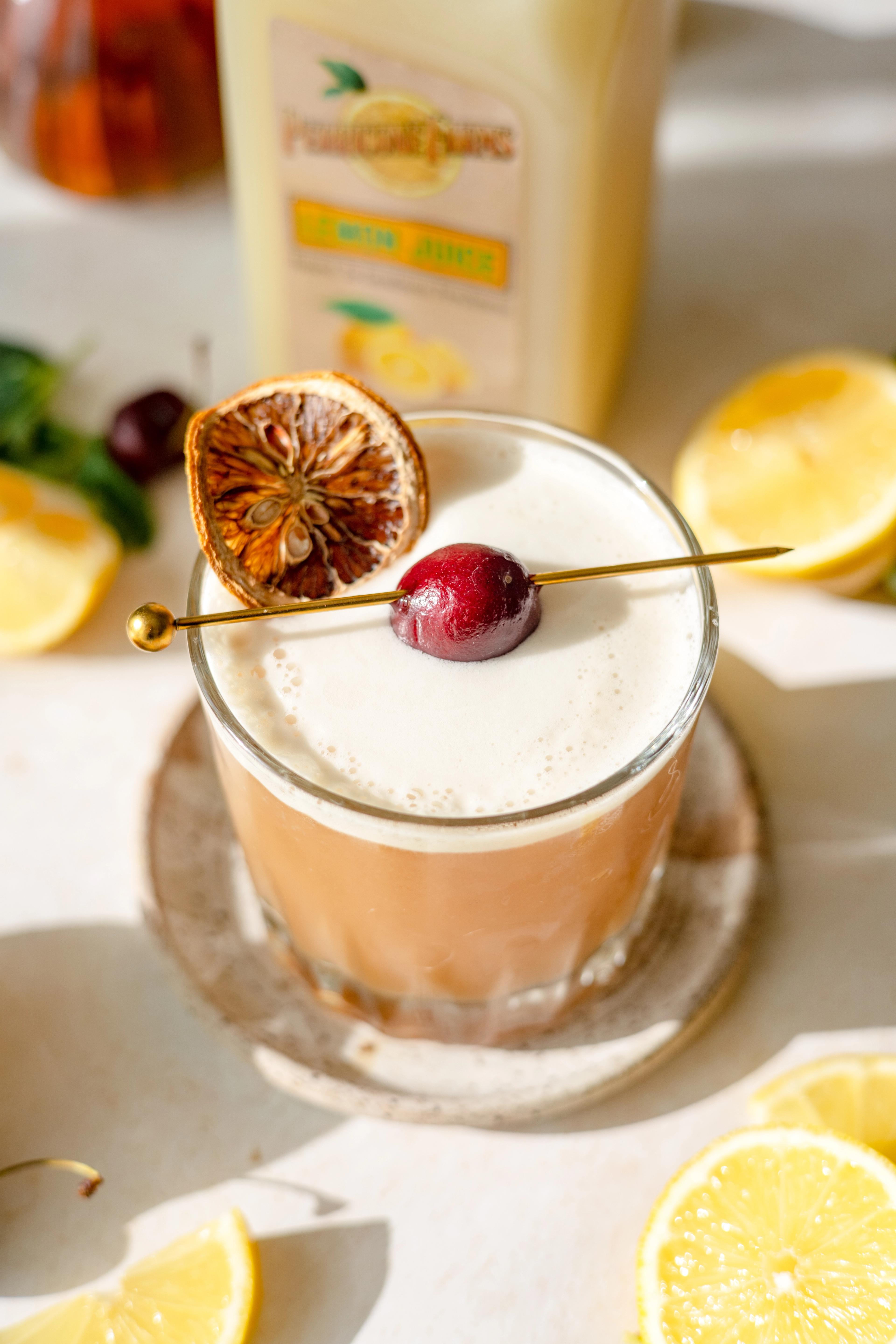 Lemon Honey Whiskey Sour made with Perricone Farms Lemon Juice, shaken with egg white and served over ice, garnished with a cherry and dehydrated lemon slice