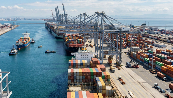 photograph taken at dawn of a bustling modern commercial port, with giant industrial cranes loading colorful shipping containers onto a massive cargo ship.