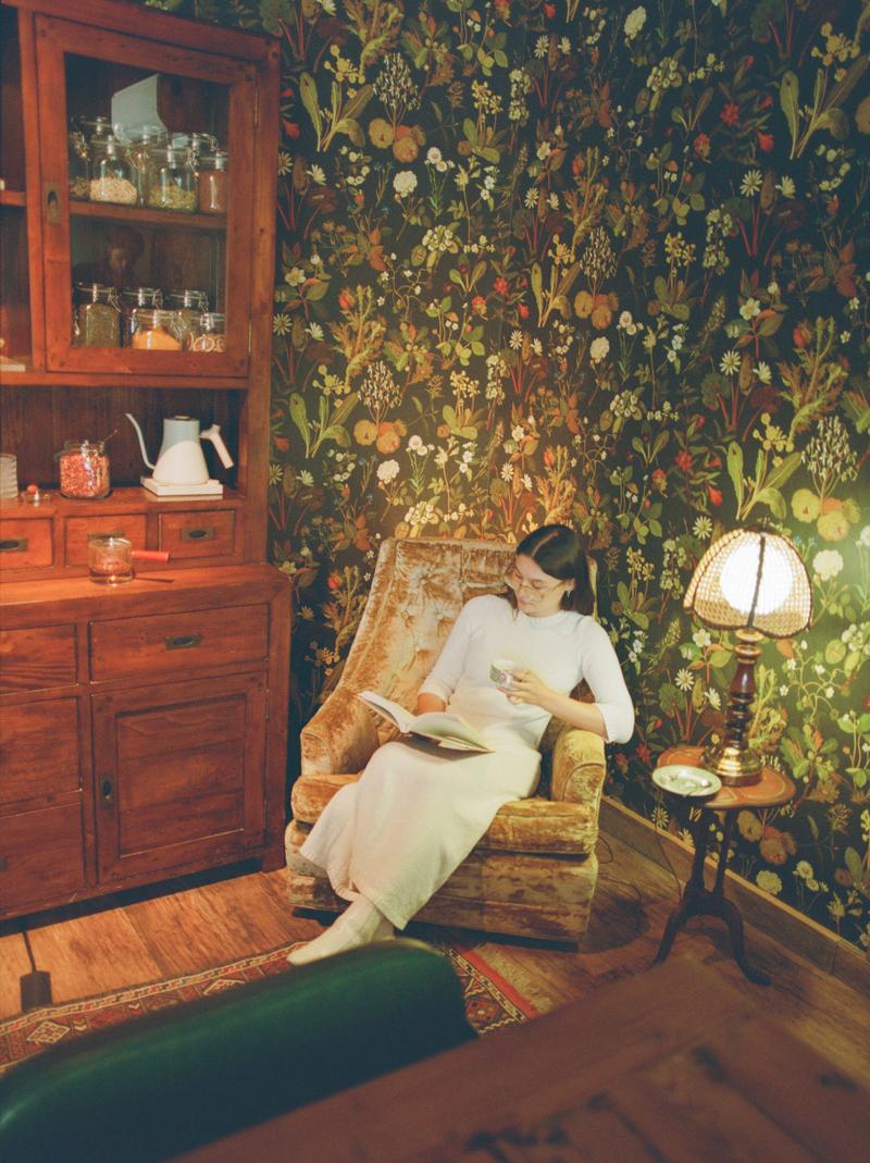 A guest reading in an armchair in the Tea Room, beside a lamp and a cabinet of tea tins.