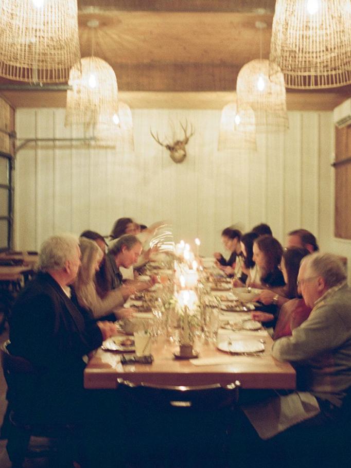Long table dinner under woven pendant lights beneath a mounted deer skull