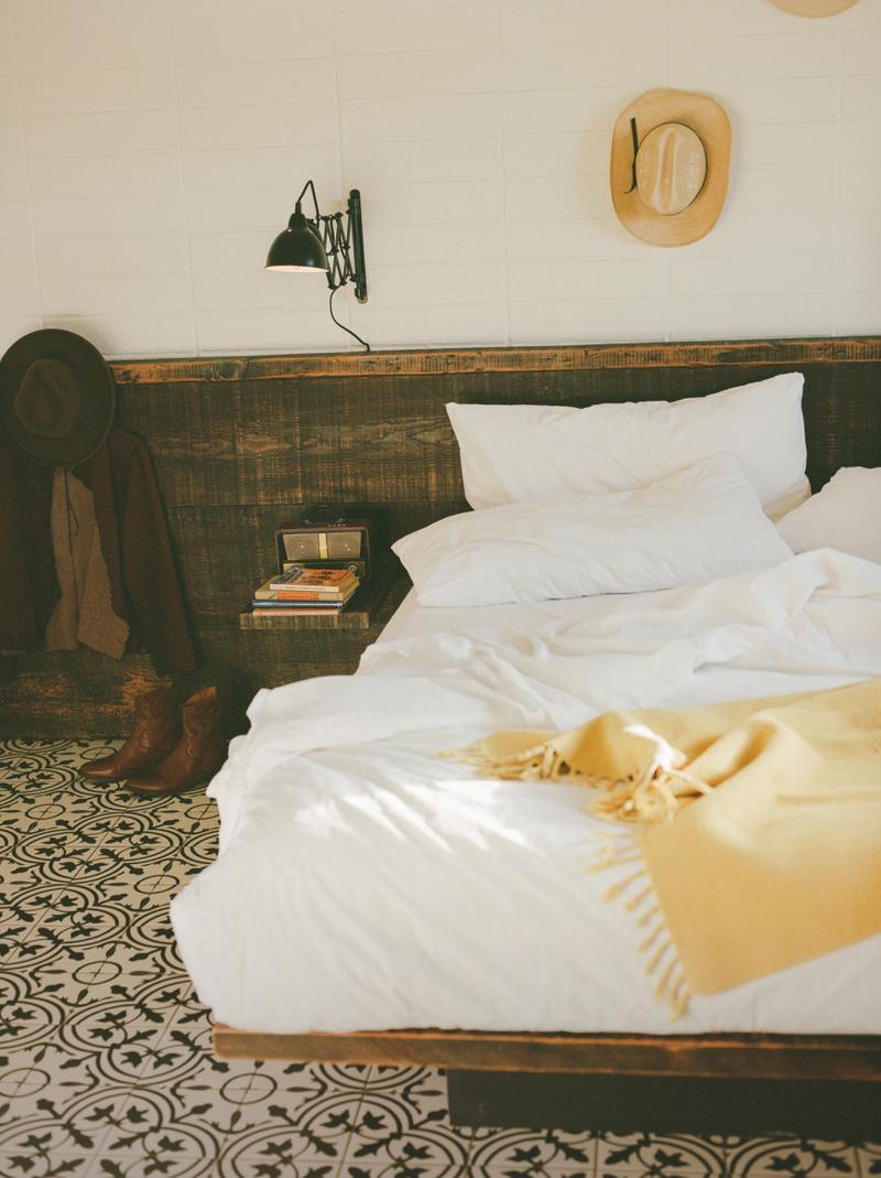A made bed with a yellow throw and a wall sconce above the patterned headboard.