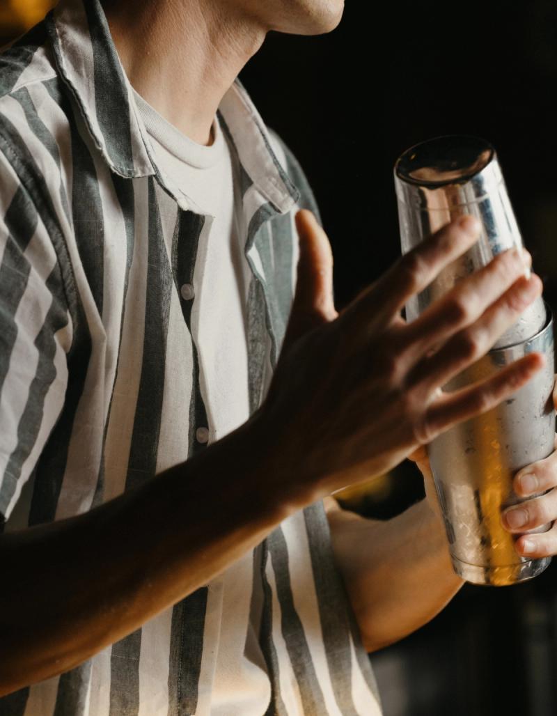 A bartender in a striped shirt holding a frosted cocktail shaker.