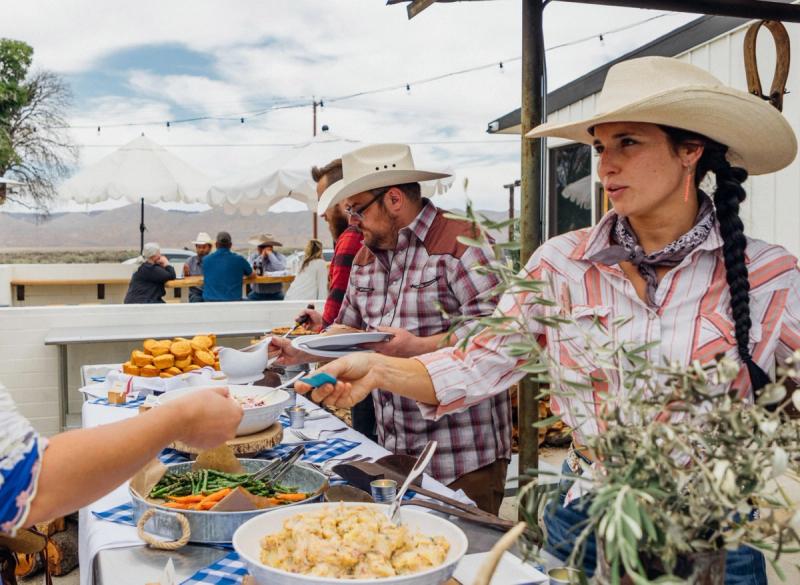 Guests in cowboy hats serving themselves from a long buffet table of BBQ and salads.