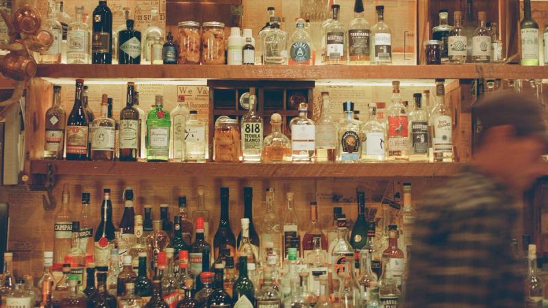 Shelves lined with bottles behind the bar, bartender at work in silhouette