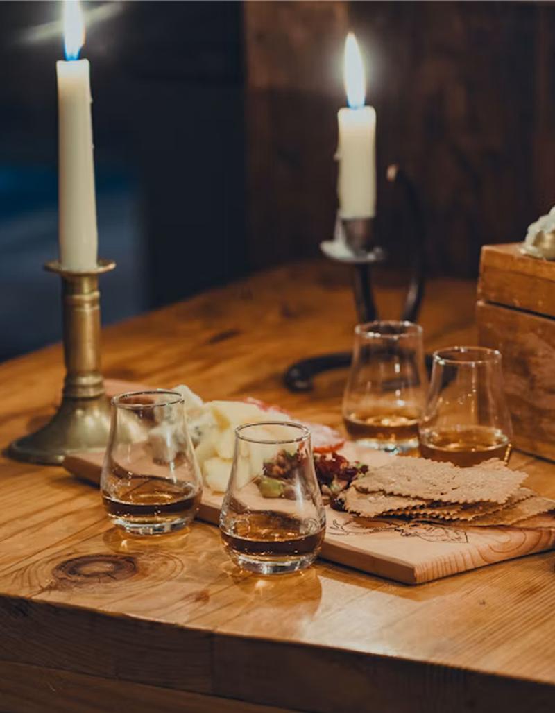 A whiskey flight sitting on a candlelit table next to a charcuterie board.
