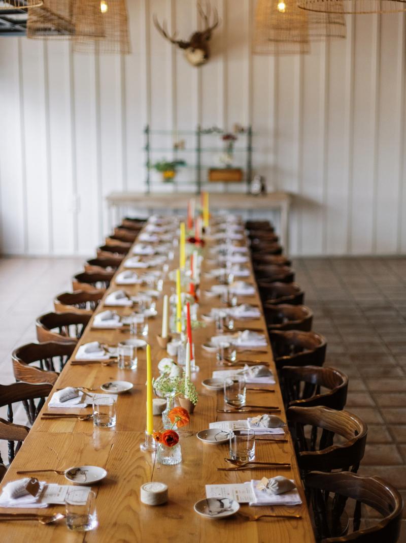 A long banquet table set with candles and small vases under antler chandeliers