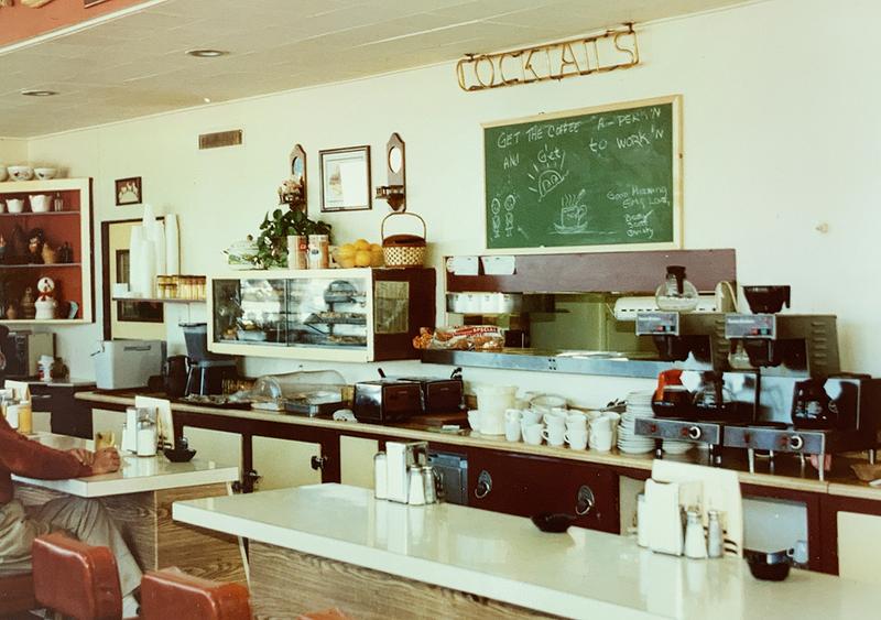 Vintage photo of the Buckhorn diner counter, with stools, an espresso machine, and a chalkboard menu beneath a "Cocktails" sign.