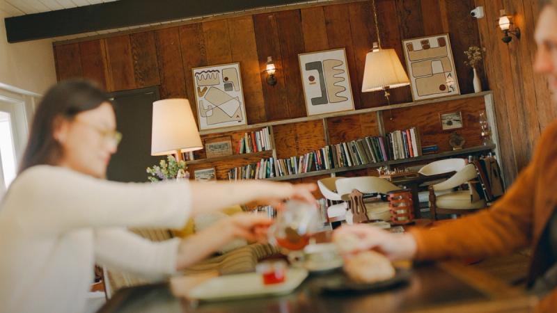 Guests seated at a wood counter being served plates in a book-lined room