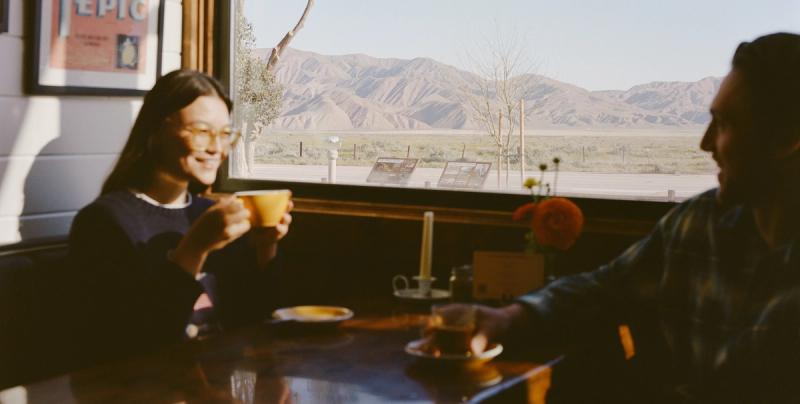Two people sharing coffee at a window table in the diner, with the mountains visible outside.