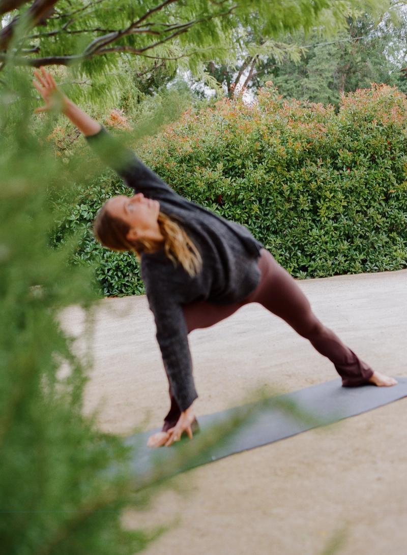 A guest in a side-angle yoga pose on a mat beneath the olive trees.