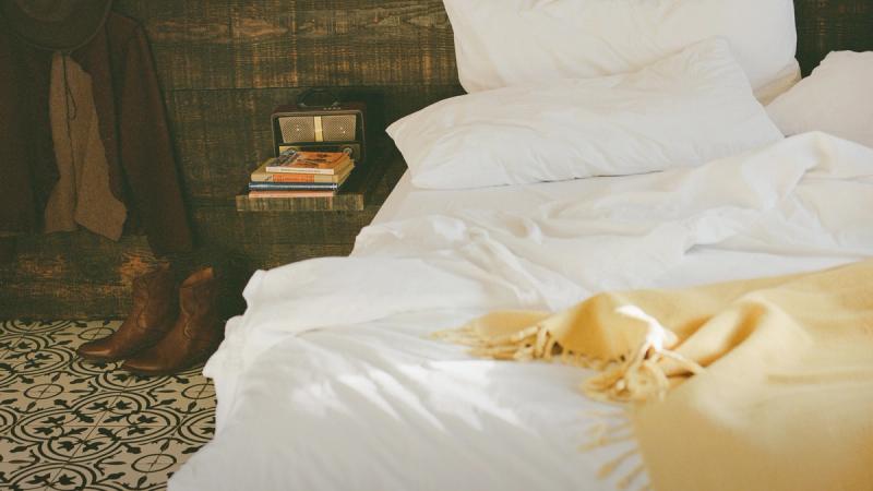 An unmade guest bed with a mustard throw and cowboy boots by the nightstand