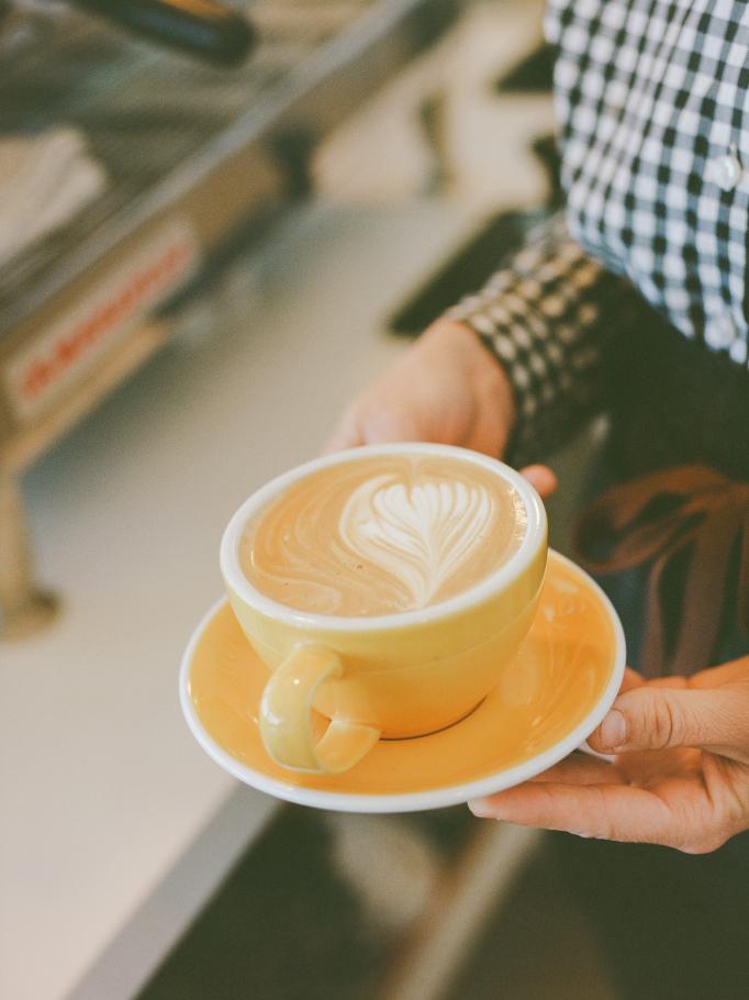 A latte with leaf-pattern foam served in a yellow cup and saucer