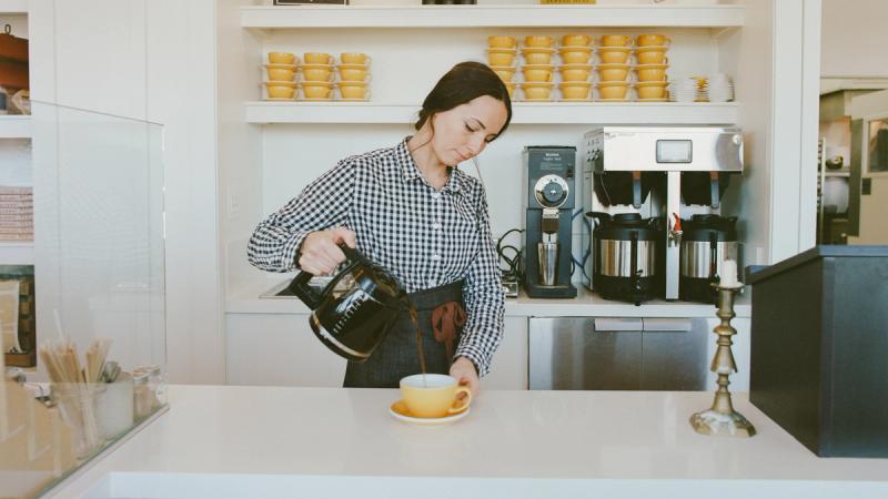 Barista pouring coffee from a kettle into a cup at the market counter