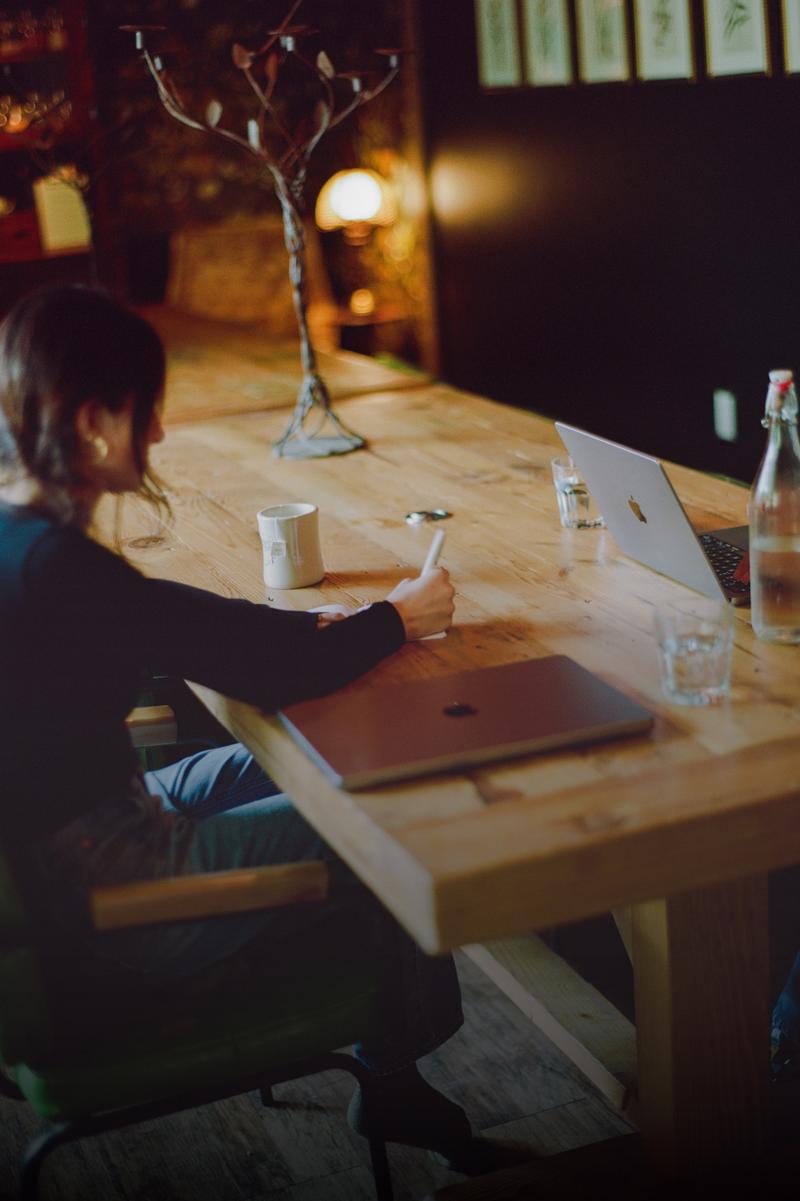 Woman working at a wood table with laptop and coffee in a dimly lit room