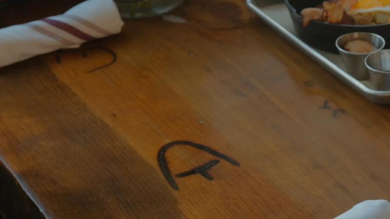 A hand-branded letter mark burned into a wooden tabletop