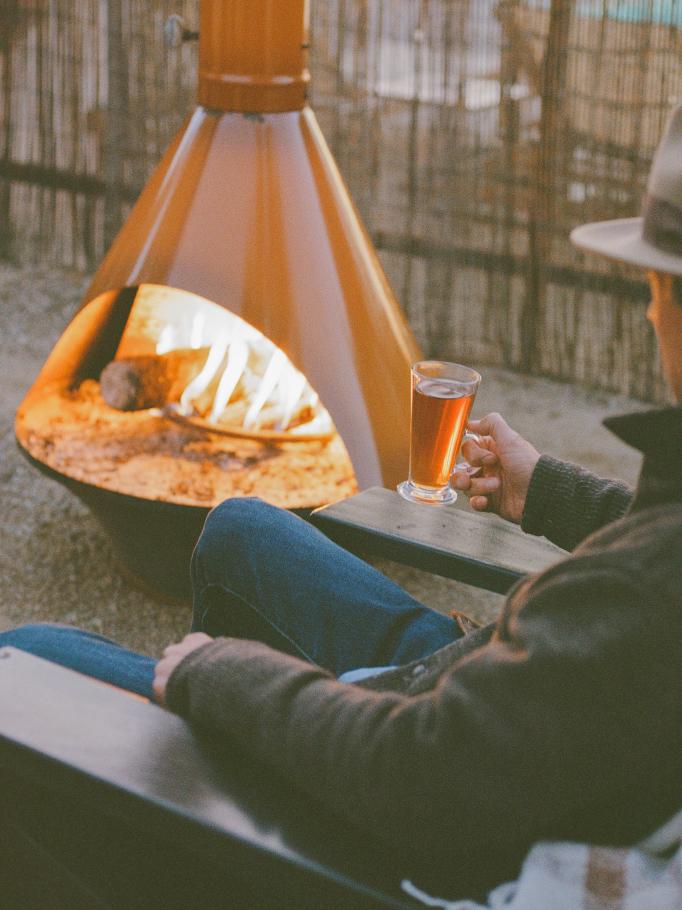 A guest warming a drink beside a lit outdoor firepit