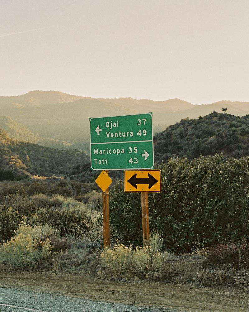 A directional highway sign pointing left to signal Ojai and Venture and pointing right to signal Maricopa and Taft