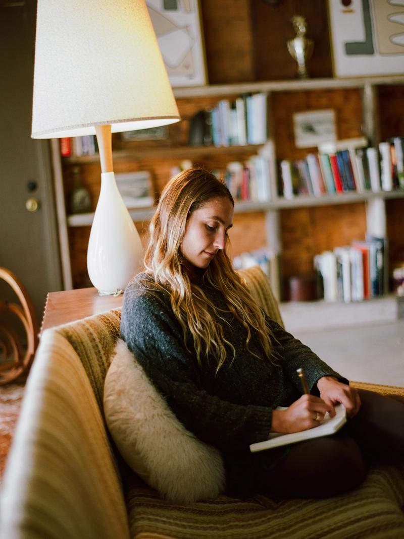 A guest journaling in the lobby, sitting on the couch below a lamp.