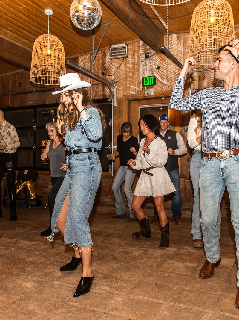 Guests line dancing under woven pendant lights and disco balls in the saloon