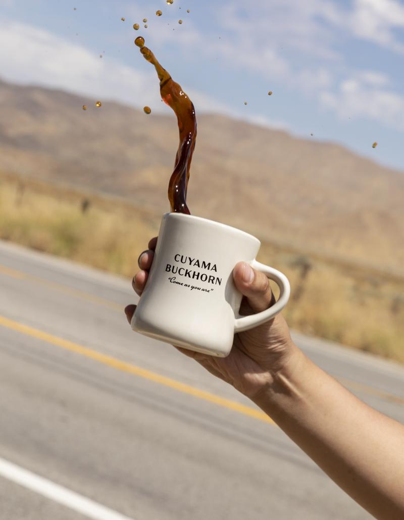 A Cuyama Buckhorn mug held up on the highway, coffee flying