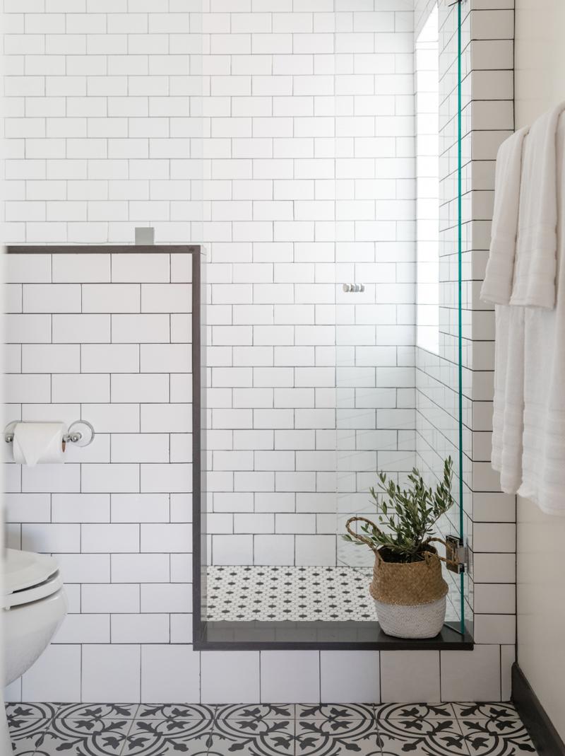 A white-tiled guest bathroom with a walk-in shower, patterned floor tile and a potted plant.